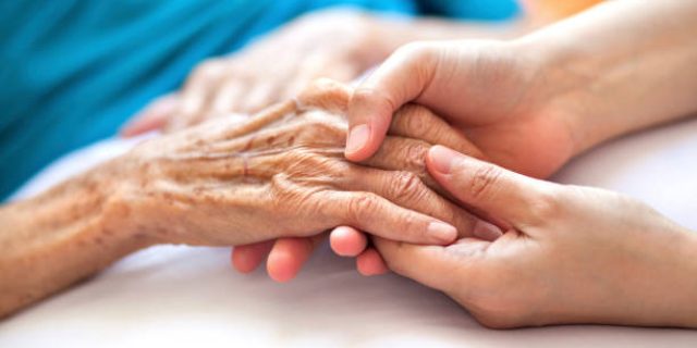 Woman holding senior woman's hand on bed